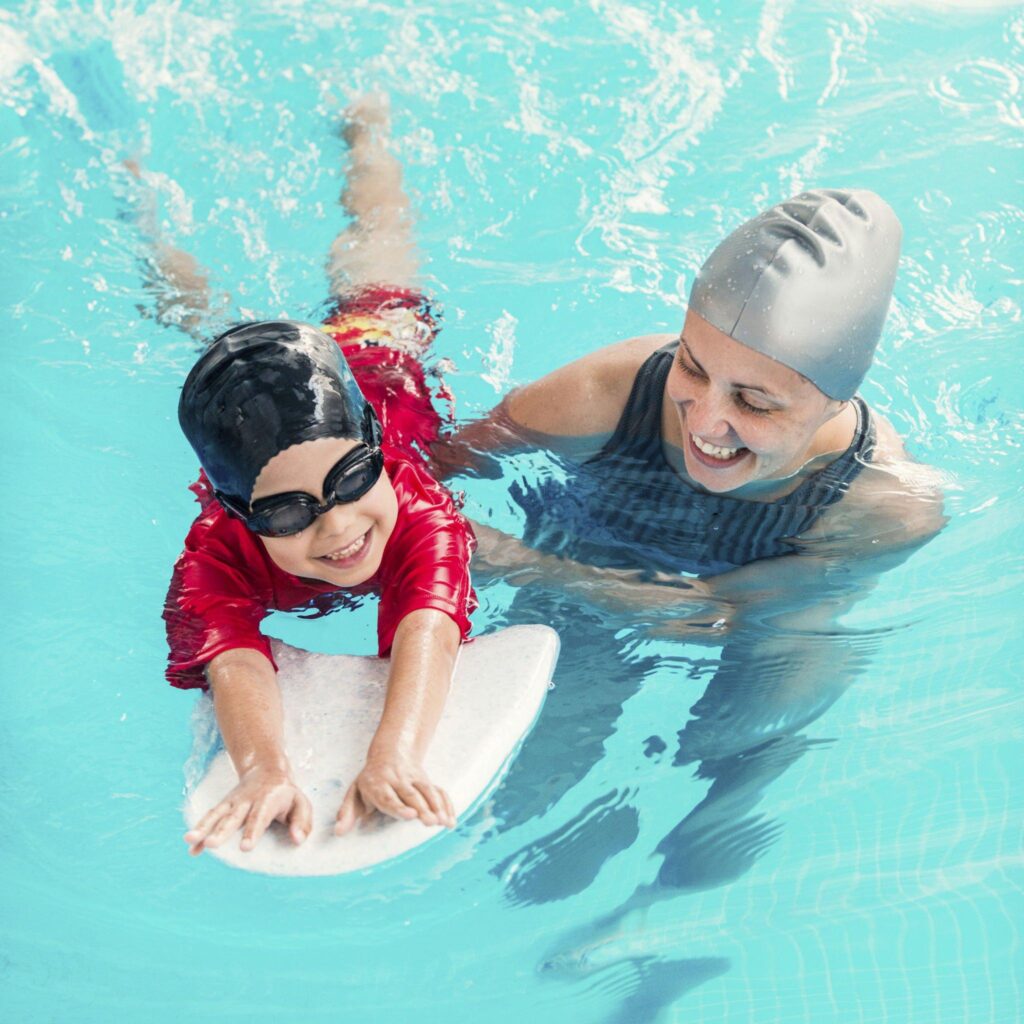 Child swimming while standing at the practice board with the coach right next to him