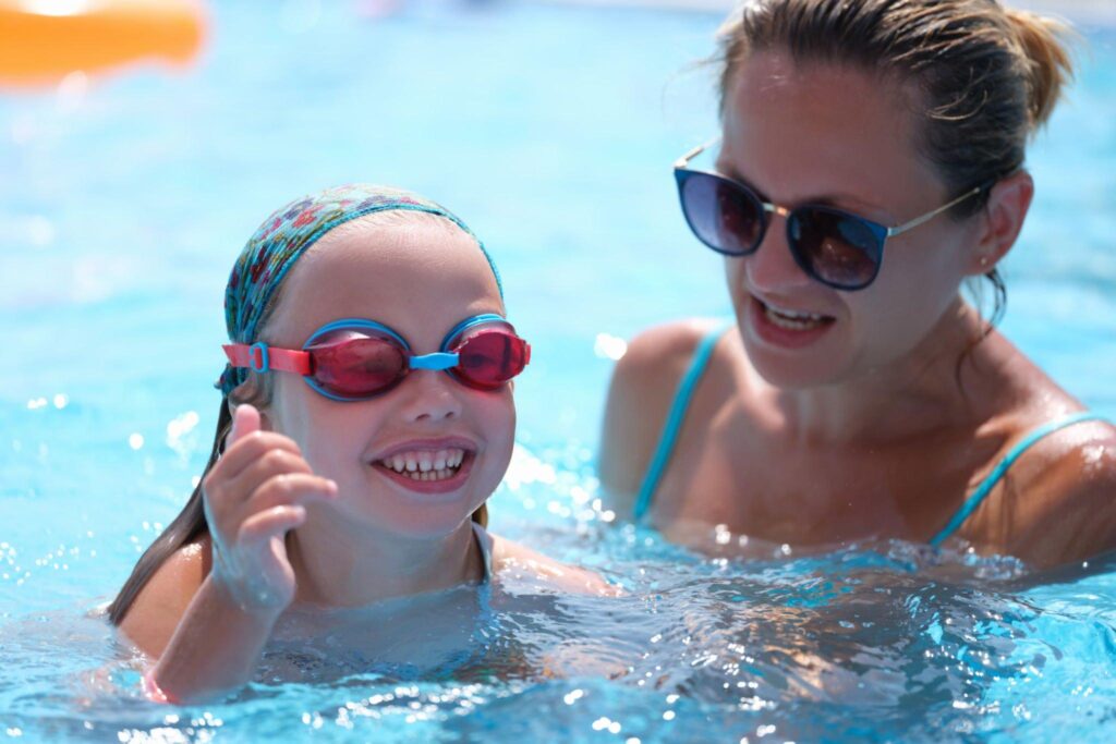 Kid with goggles enjoying her swim session with her swim coach next to her