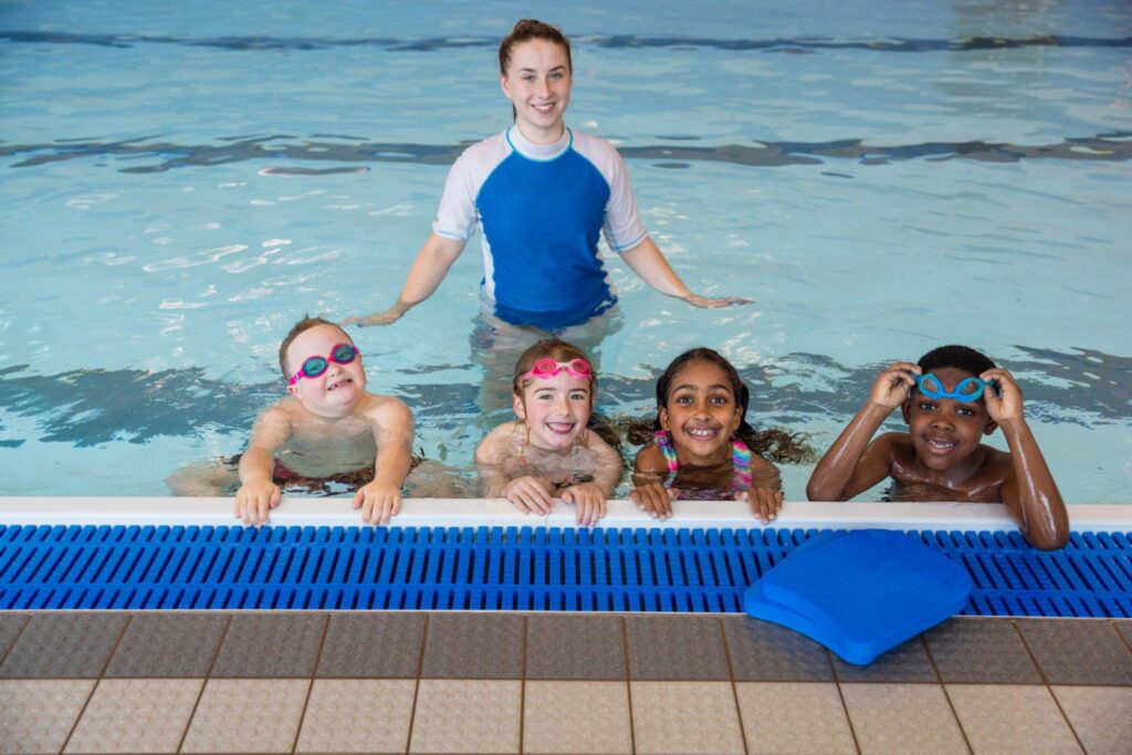 Group of kids enjoying their swimming session with the coach standing right behind them